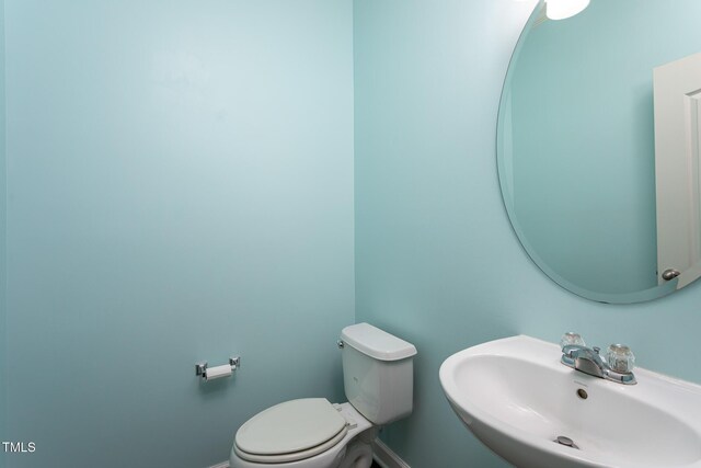 half bath featuring a sink, toilet, and baseboards