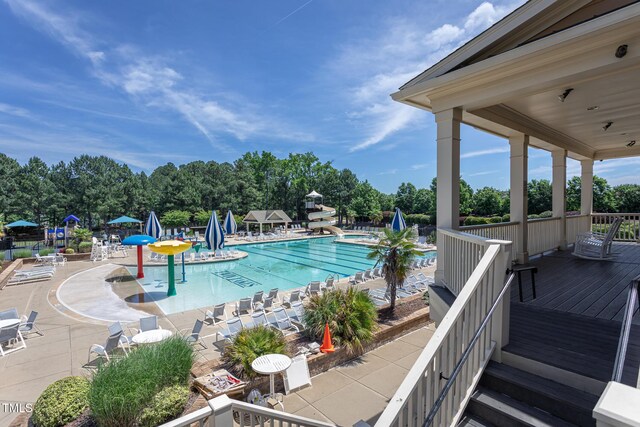 community pool featuring view of scattered trees, a deck, and a patio