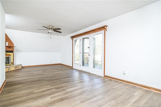 unfurnished living room featuring baseboards, wood finished floors, a ceiling fan, a glass covered fireplace, and a textured ceiling