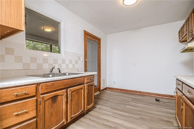 kitchen featuring a sink, light wood finished floors, brown cabinets, backsplash, and light countertops