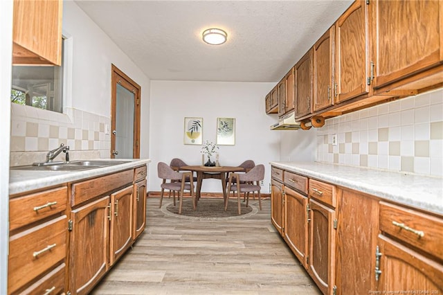 kitchen with a sink, brown cabinetry, backsplash, light countertops, and a textured ceiling
