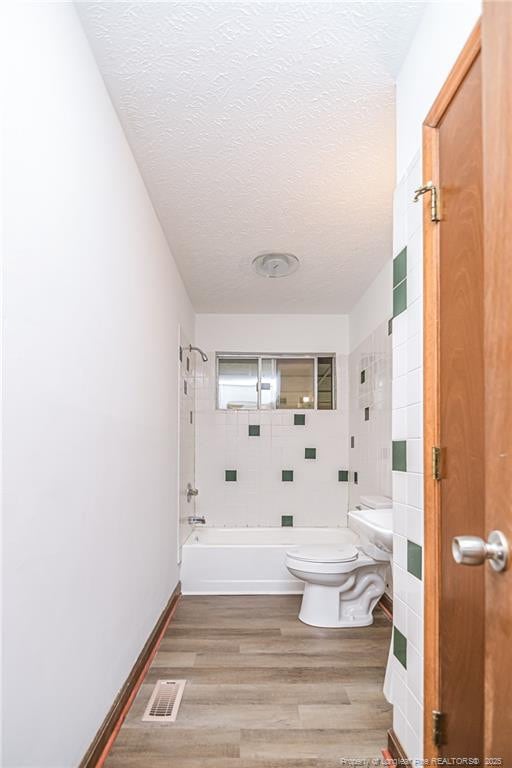 bathroom featuring toilet, bathing tub / shower combination, wood finished floors, and a textured ceiling