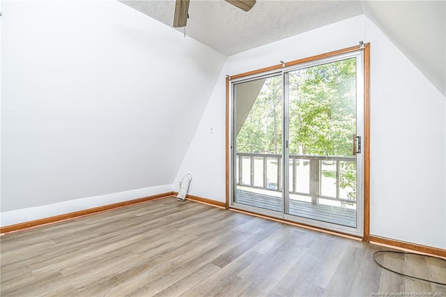 additional living space featuring wood finished floors, vaulted ceiling, baseboards, ceiling fan, and a textured ceiling