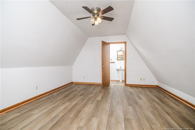 bonus room featuring ceiling fan, light wood-style flooring, vaulted ceiling, baseboards, and a sink