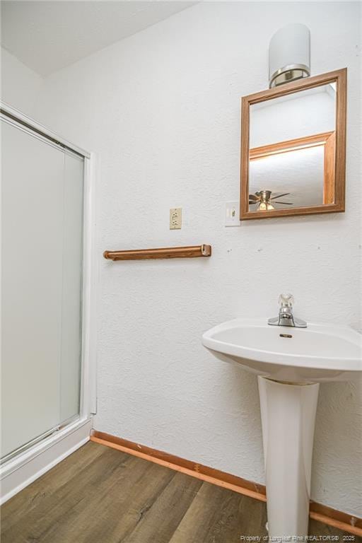 bathroom with wood finished floors, baseboards, a sink, and a shower with shower door