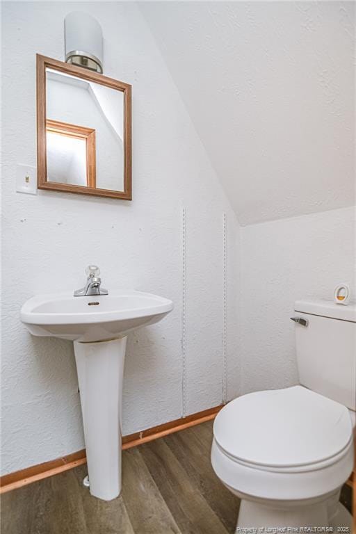 bathroom featuring wood finished floors, vaulted ceiling, toilet, baseboards, and a sink
