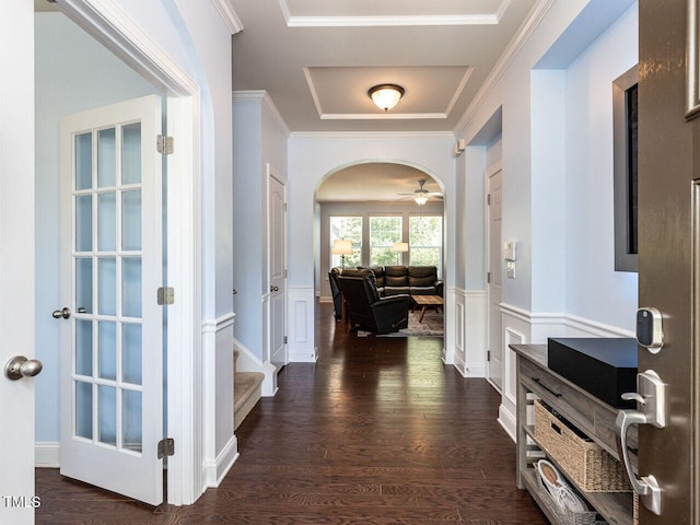 hall with arched walkways, dark wood finished floors, a raised ceiling, crown molding, and wainscoting