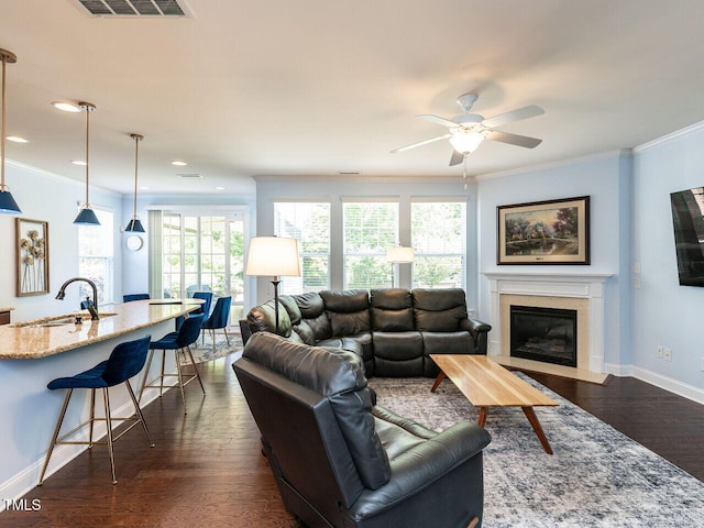 living room with dark wood-style flooring, ornamental molding, a ceiling fan, a fireplace with flush hearth, and baseboards