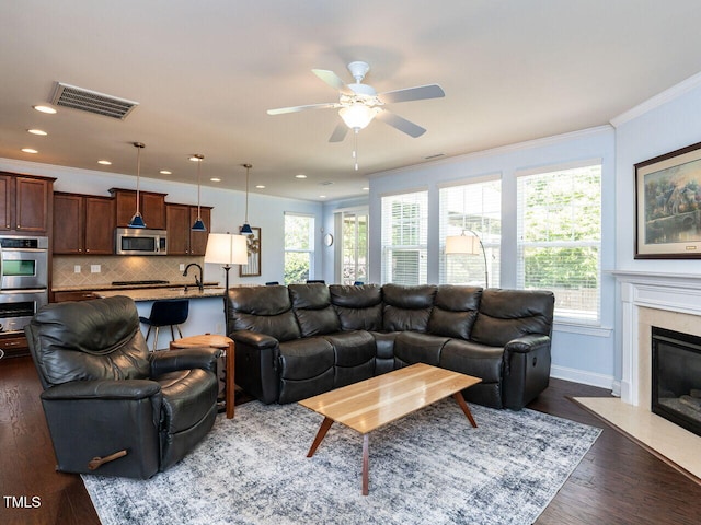 living room featuring plenty of natural light, dark wood-style floors, a ceiling fan, crown molding, and a fireplace