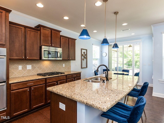 kitchen with a sink, stainless steel microwave, gas stovetop, dark wood finished floors, and a center island with sink