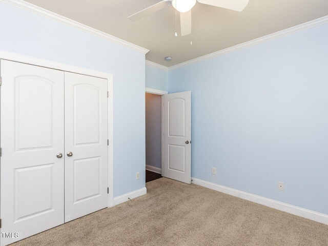 unfurnished bedroom featuring carpet, ornamental molding, baseboards, a closet, and a ceiling fan