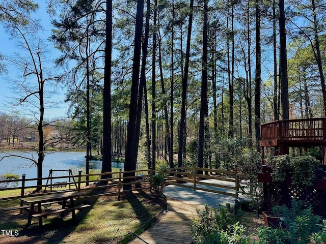 surrounding community with a deck with water view, fence, and a forest view