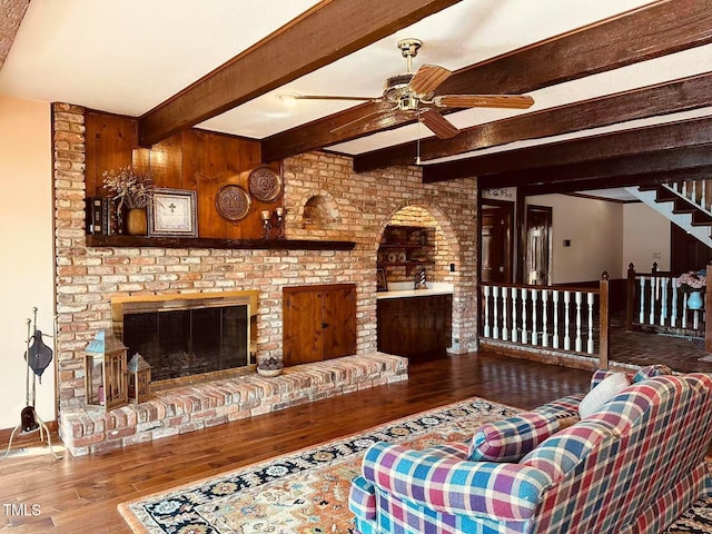 living room featuring hardwood / wood-style flooring, beamed ceiling, a ceiling fan, and a brick fireplace