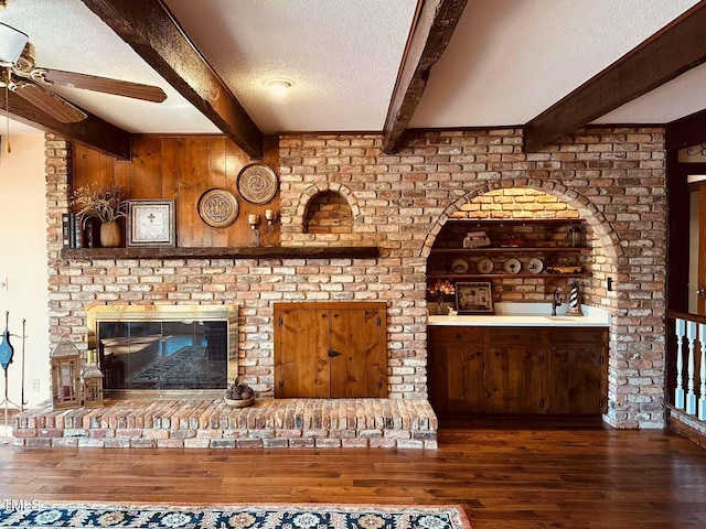 unfurnished living room featuring beamed ceiling, hardwood / wood-style floors, a textured ceiling, ceiling fan, and a fireplace