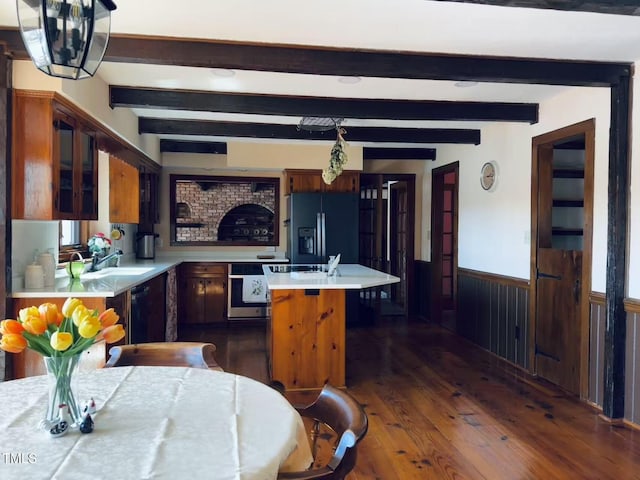 kitchen featuring black refrigerator with ice dispenser, light countertops, a wainscoted wall, stainless steel oven, and dark wood-type flooring