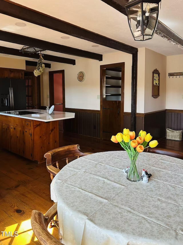 dining room with a wainscoted wall, wood finished floors, and beam ceiling