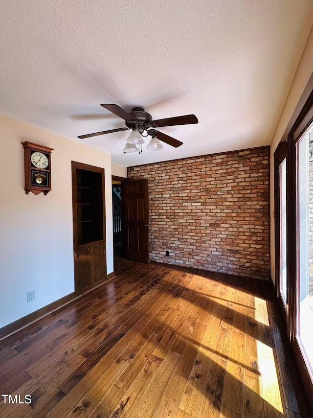empty room with brick wall, ceiling fan, wood-type flooring, a textured ceiling, and baseboards