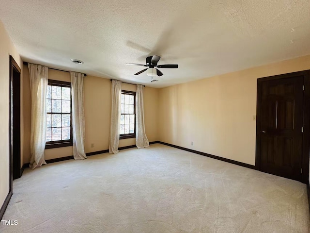 spare room with light carpet, a ceiling fan, a textured ceiling, and baseboards