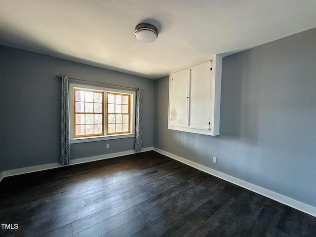 empty room with dark wood-style flooring and baseboards