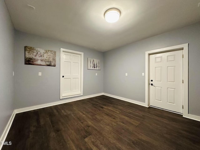 spare room featuring baseboards and dark wood-type flooring