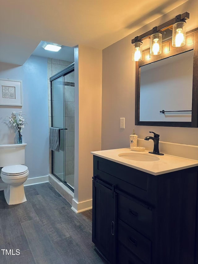 bathroom featuring wood finished floors, a shower stall, toilet, and vanity