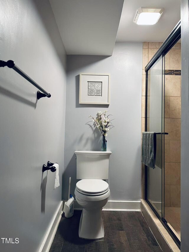 bathroom with baseboards, a stall shower, toilet, and wood finished floors