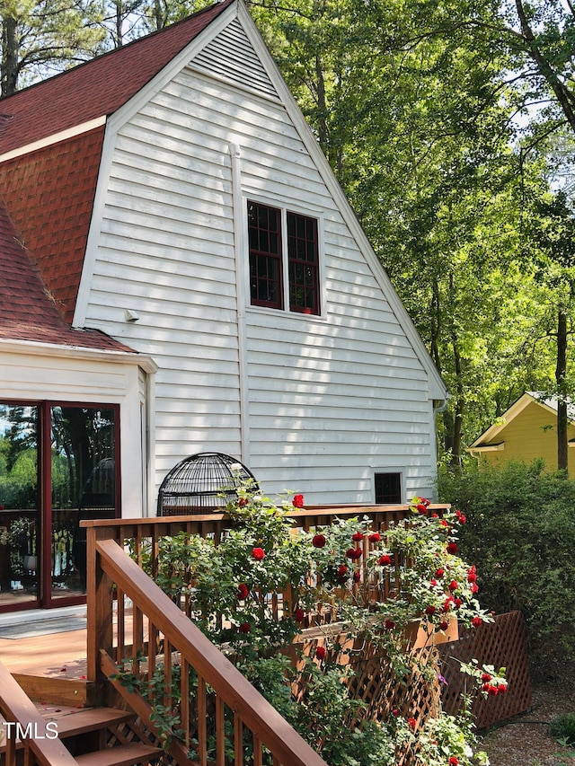 view of side of property with a shingled roof and a wooden deck