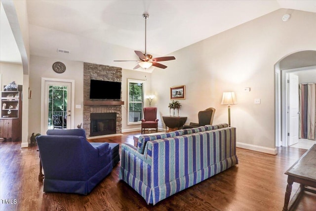 living room featuring vaulted ceiling, baseboards, wood finished floors, a stone fireplace, and ceiling fan