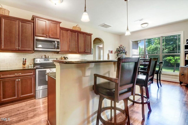 kitchen with stainless steel appliances, light wood-type flooring, a breakfast bar, decorative backsplash, and pendant lighting