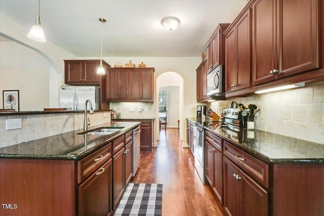 kitchen with appliances with stainless steel finishes, arched walkways, a sink, tasteful backsplash, and dark wood-style flooring