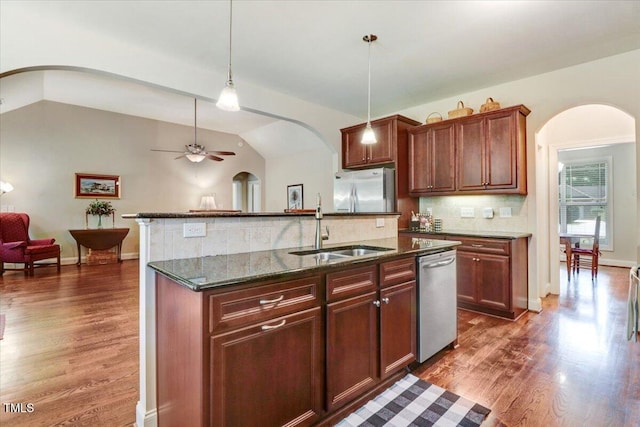 kitchen with appliances with stainless steel finishes, arched walkways, a sink, dark wood-type flooring, and decorative backsplash