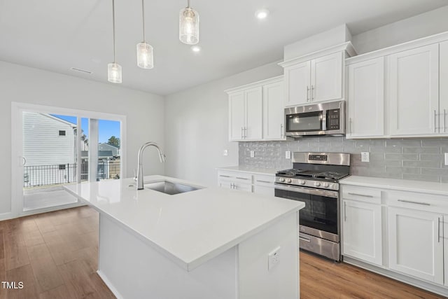 kitchen with stainless steel appliances, a sink, backsplash, light wood-style floors, and a center island with sink