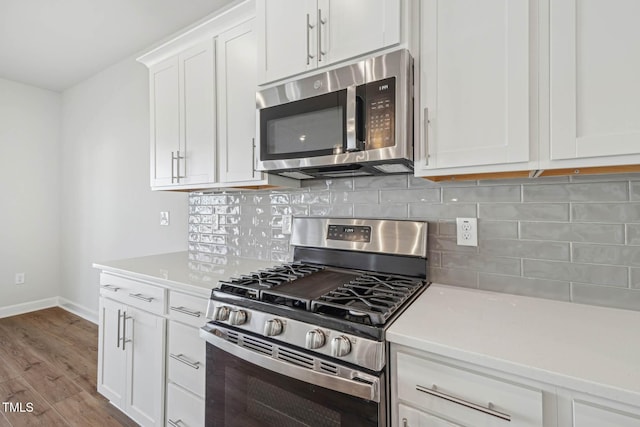 kitchen with appliances with stainless steel finishes, light countertops, white cabinets, baseboards, and wood finished floors