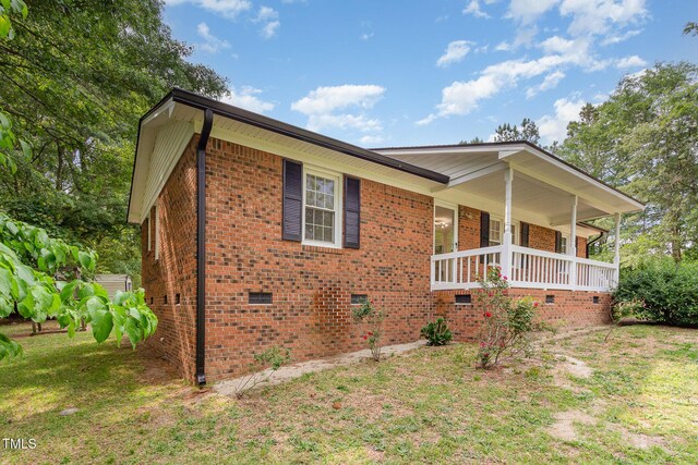 view of side of property with crawl space, brick siding, and a porch
