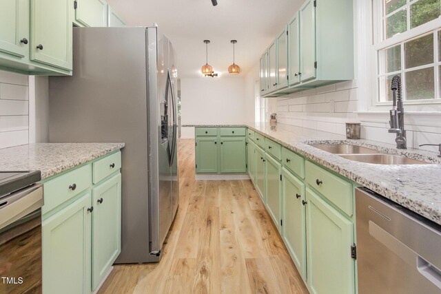 kitchen with a sink, stainless steel appliances, green cabinetry, and light wood finished floors