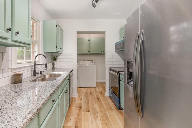 kitchen with appliances with stainless steel finishes, green cabinets, washer / dryer, and a sink