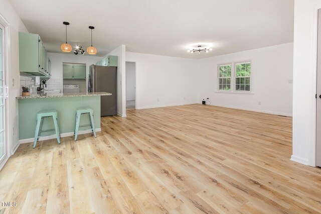kitchen featuring green cabinetry, freestanding refrigerator, a peninsula, light wood-type flooring, and a kitchen bar