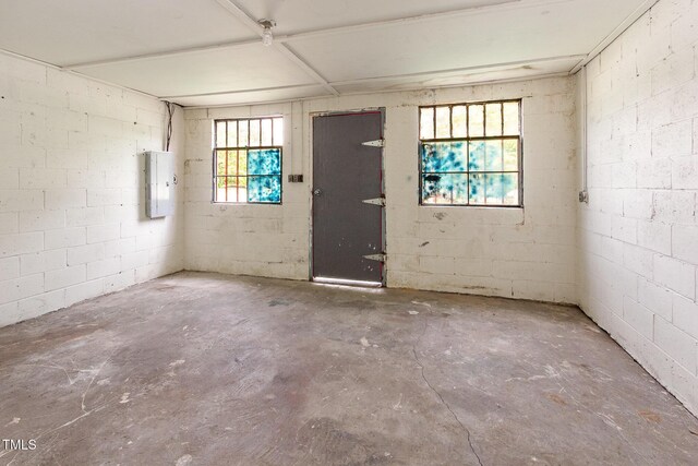 spare room featuring unfinished concrete flooring, concrete block wall, and electric panel