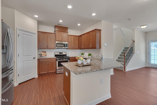 kitchen with stainless steel appliances, wood finished floors, a sink, baseboards, and backsplash