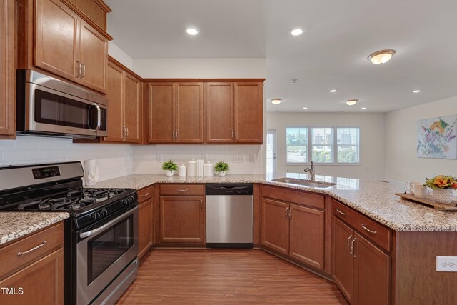 kitchen with appliances with stainless steel finishes, a sink, a peninsula, light wood finished floors, and tasteful backsplash