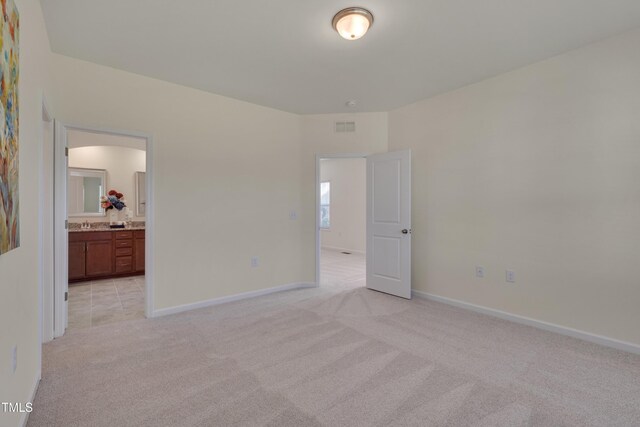 unfurnished bedroom with light colored carpet, baseboards, and ensuite bathroom