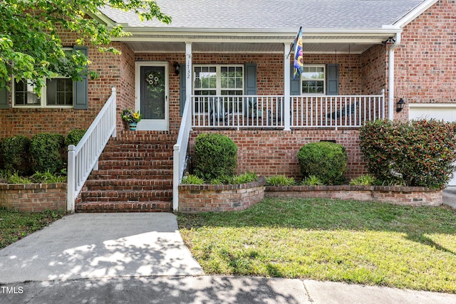 view of exterior entry featuring brick siding, a yard, covered porch, and roof with shingles