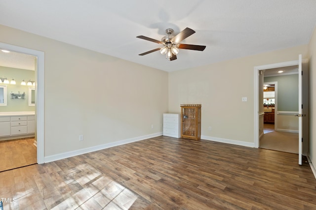 unfurnished bedroom featuring wood finished floors, baseboards, ensuite bathroom, and ceiling fan