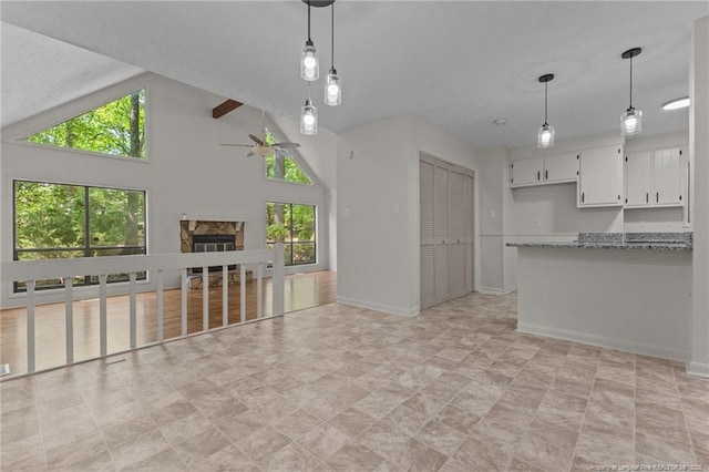 unfurnished living room featuring a stone fireplace, ceiling fan, baseboards, and lofted ceiling