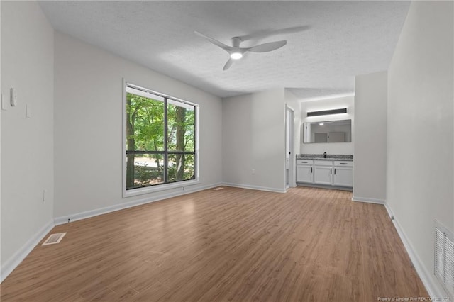 unfurnished living room with a textured ceiling, light wood-style floors, a ceiling fan, and baseboards