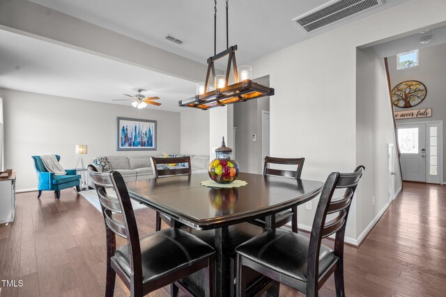 dining space with dark wood-type flooring, a chandelier, a ceiling fan, and baseboards