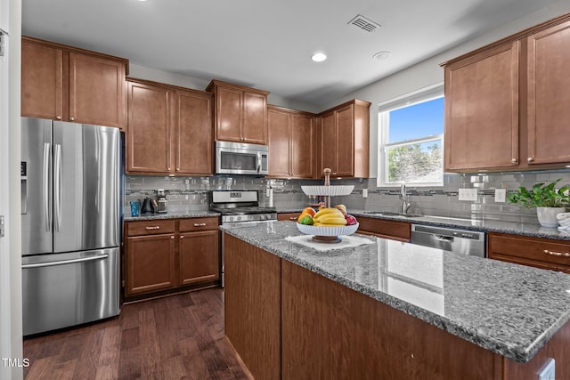 kitchen with stainless steel appliances, dark wood-style flooring, a sink, stone counters, and tasteful backsplash