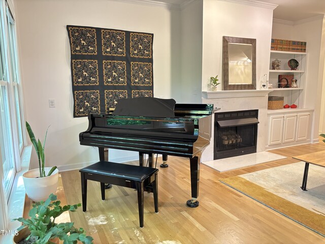 living area with wood finished floors, ornamental molding, a fireplace with raised hearth, built in features, and baseboards