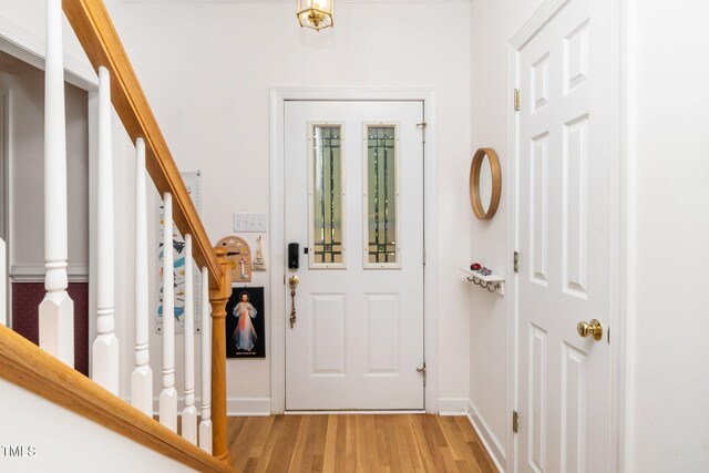 foyer entrance with light wood-style flooring, stairway, and baseboards