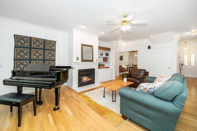 living area featuring crown molding, wood finished floors, a ceiling fan, a fireplace with flush hearth, and built in shelves